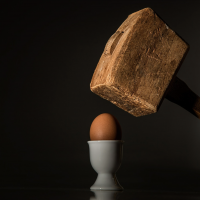 Marteau en bois s'apprêtant à frapper un oeuf dans un coquetier